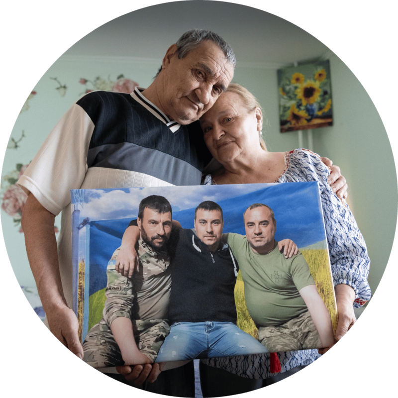 An older couple in Ukraine pose with a photo of their three adult sons