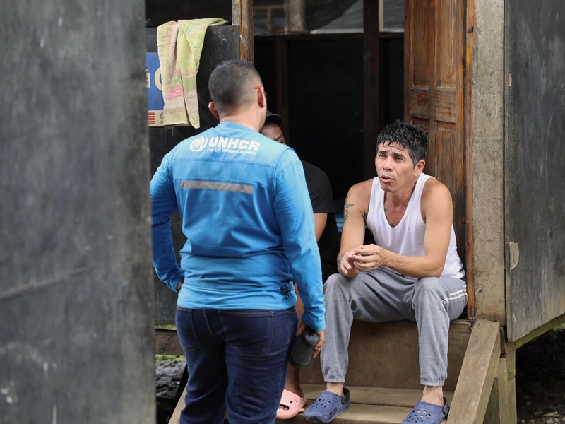 Owar, who fled Venezuela in search of a better life, sits on steps outside a shelter speaks with a UNHCR staff member.