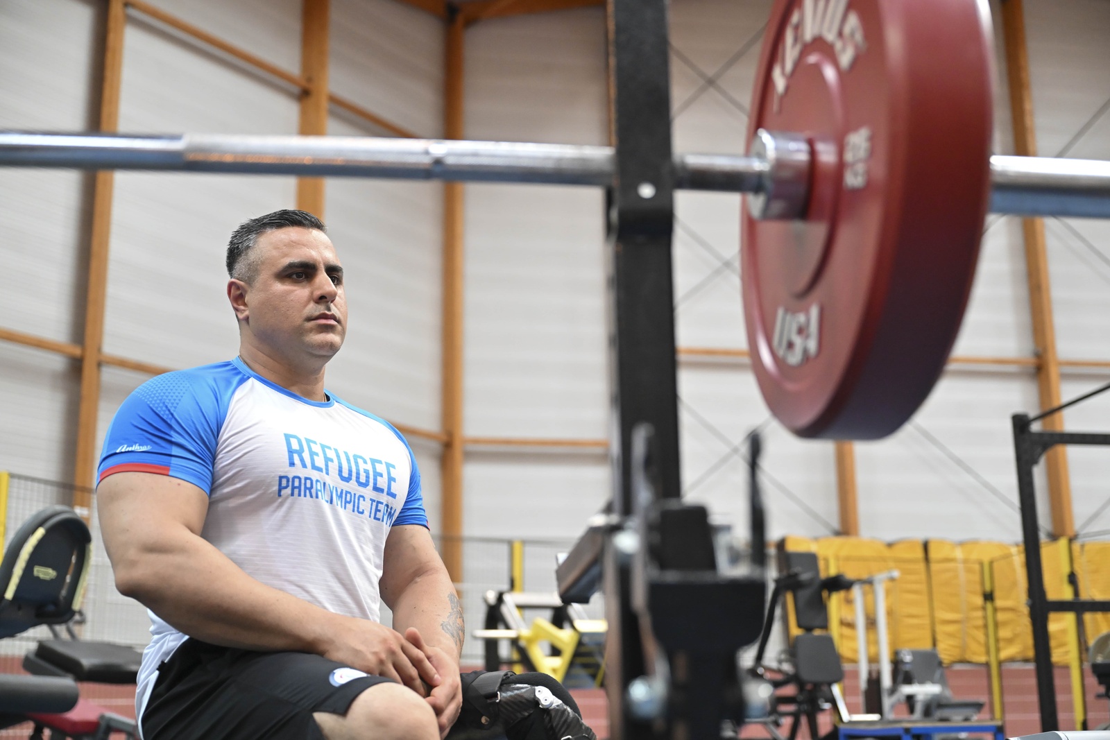 A man sits while looking at a barbell with weights