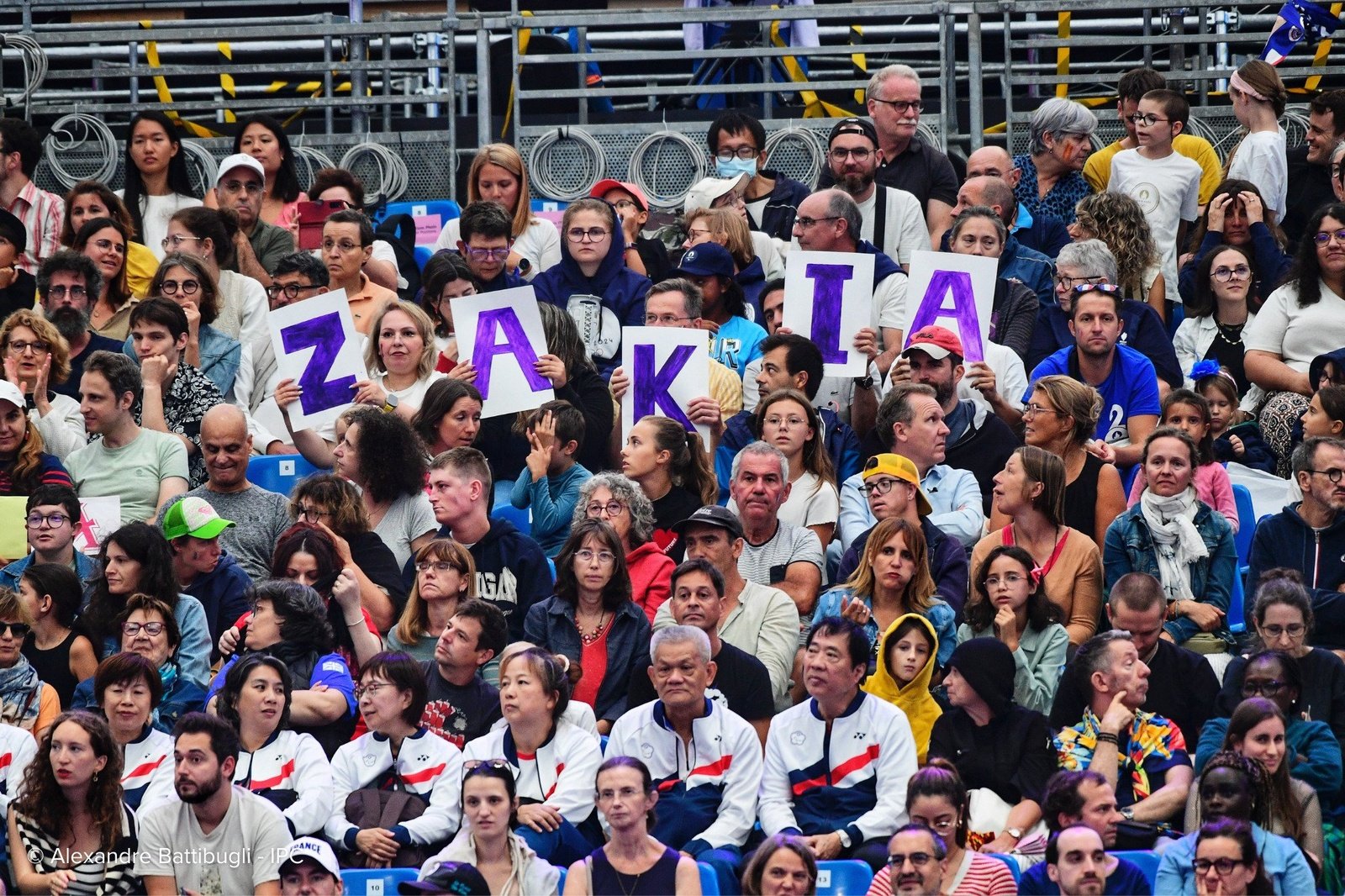 Members of a large crowd hold up handmade signs with letters spelling out Zakia.