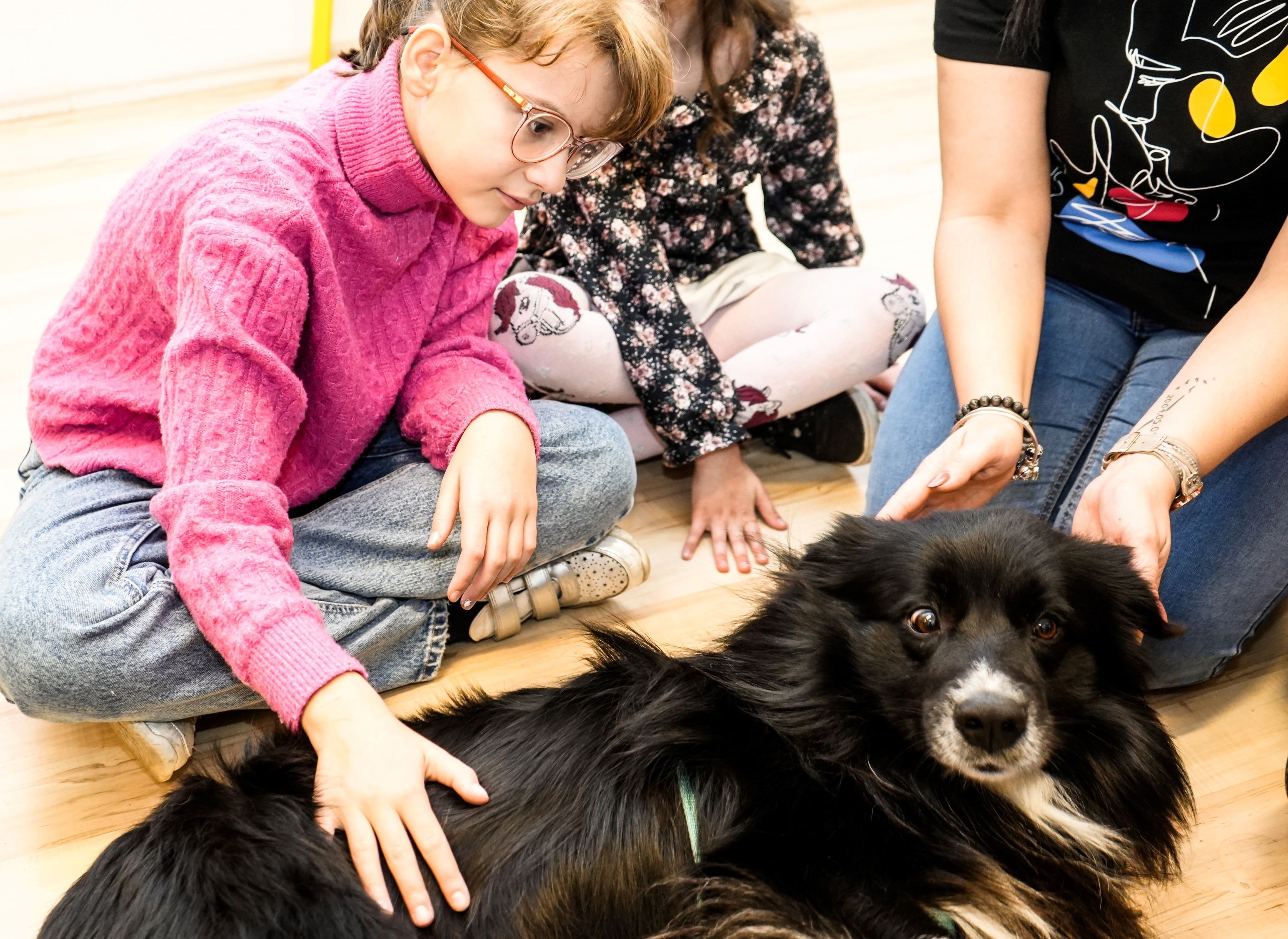 Ukrainian refugee children Yuliya (pink jumper) and Maria (floral dress) are in an animal therapy session at the UNHCR-supported Budapest Helps! community centre in Hungary. Noir, the dog, is specially trained to calm the children. © UNHCR/Zsolt Balla