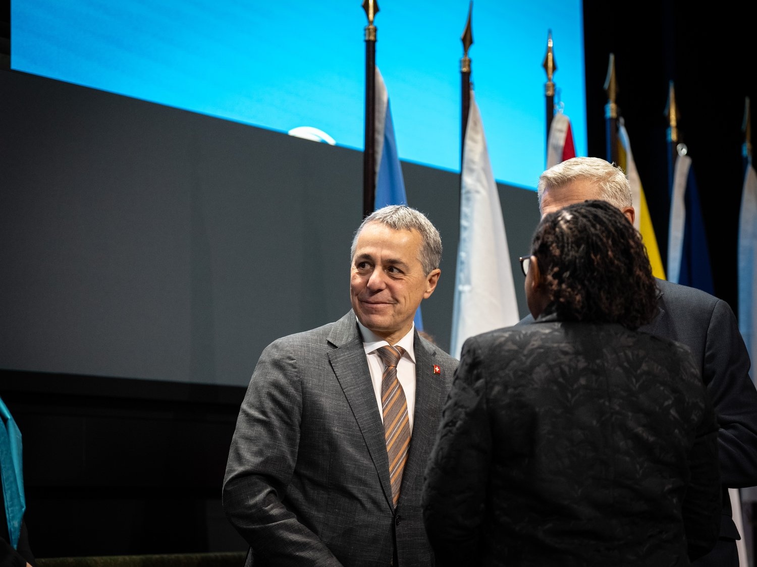 A man in a suit smiles as two people stand to his left