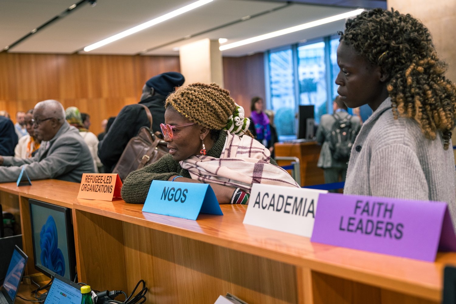 People stand behind a counter displaying delegation signs in a conference venue