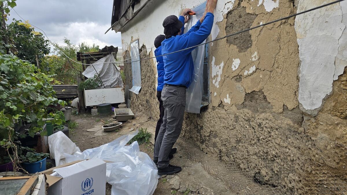 Two men install plastic sheeting over the external window of a damaged building