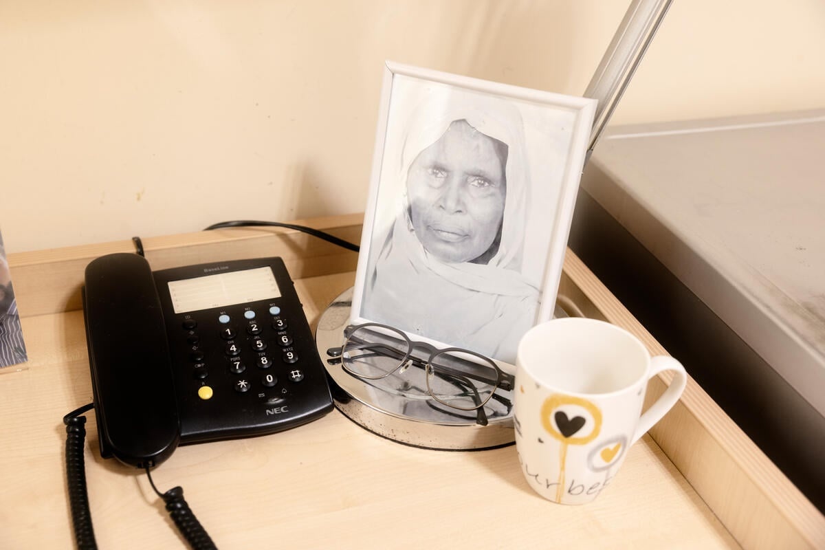 A framed black and white photo of an older woman sits on a desk next to a phone, amug and a pair of reading glasses