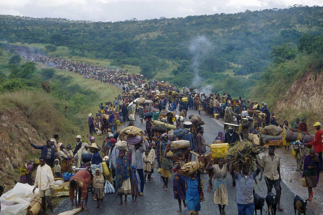 A large group of Rwandan refugees walk on a road through the country side