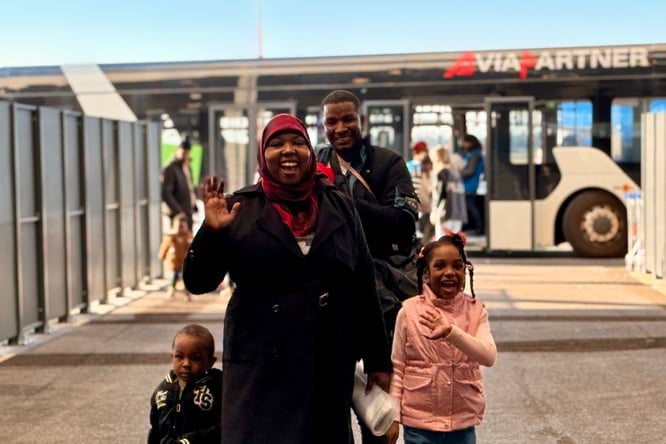 A smiling family in front of an airport shuttle bus