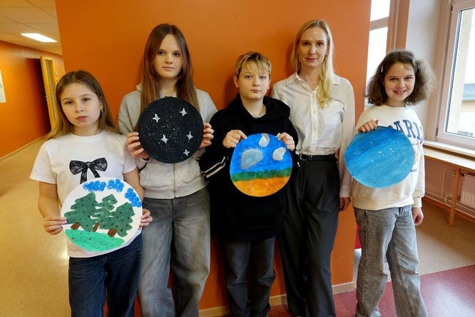 Four children pose with artwork alongside an adult woman