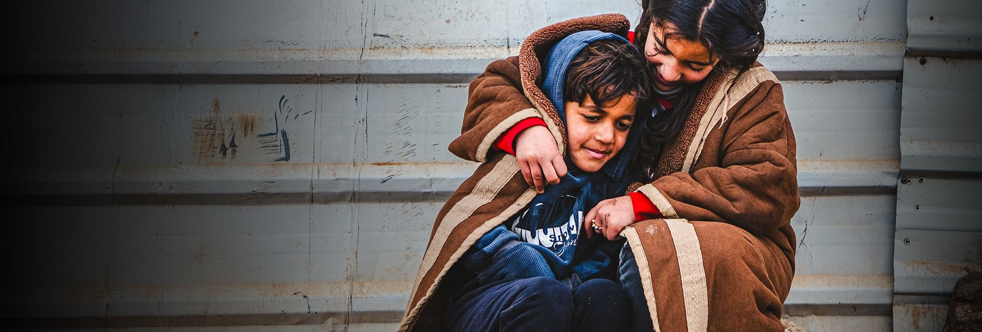 A young Syrian refugee wraps herself and her younger brother in a blanket as they sit outside in the cold in the Zaatari refugee camp.