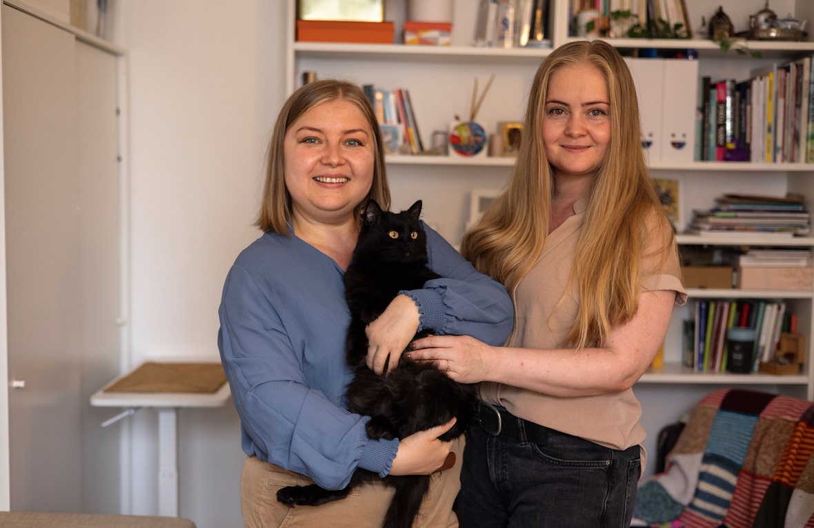 Anastasiia (left) stands with her sister Tania and their cat Kotya, at their home in Paris, France.