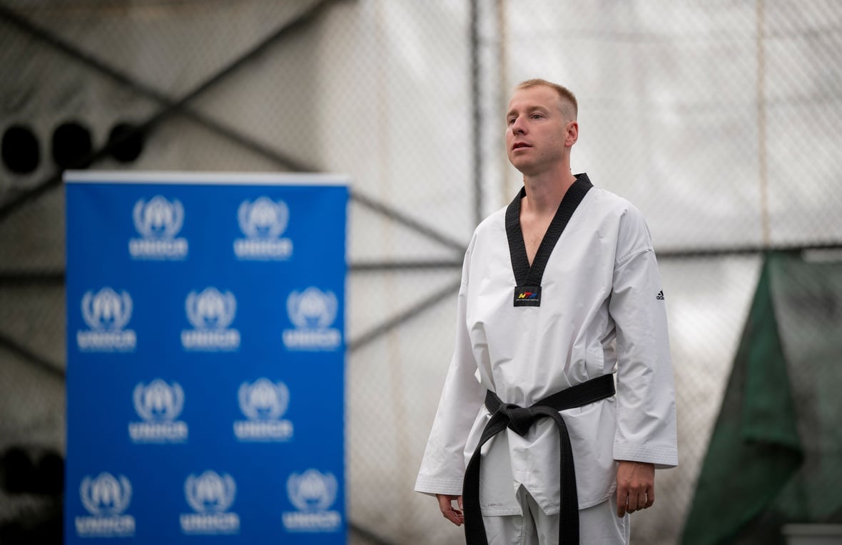 A man wearing a taekwondo outfit standing next to a UNHCR banner.