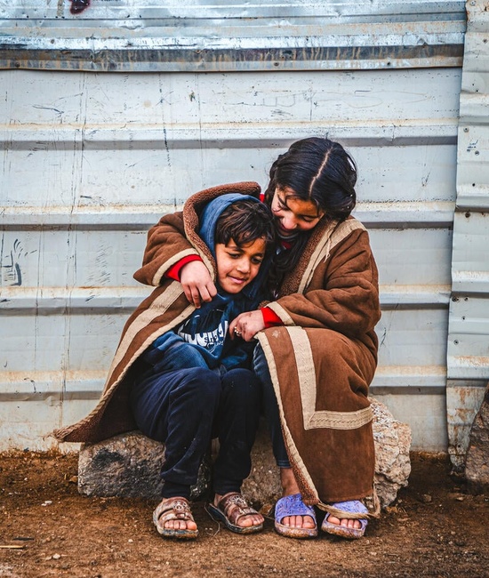 A young Syrian refugee wraps herself and her younger brother in a blanket as they sit outside in the cold in the Zaatari refugee camp.