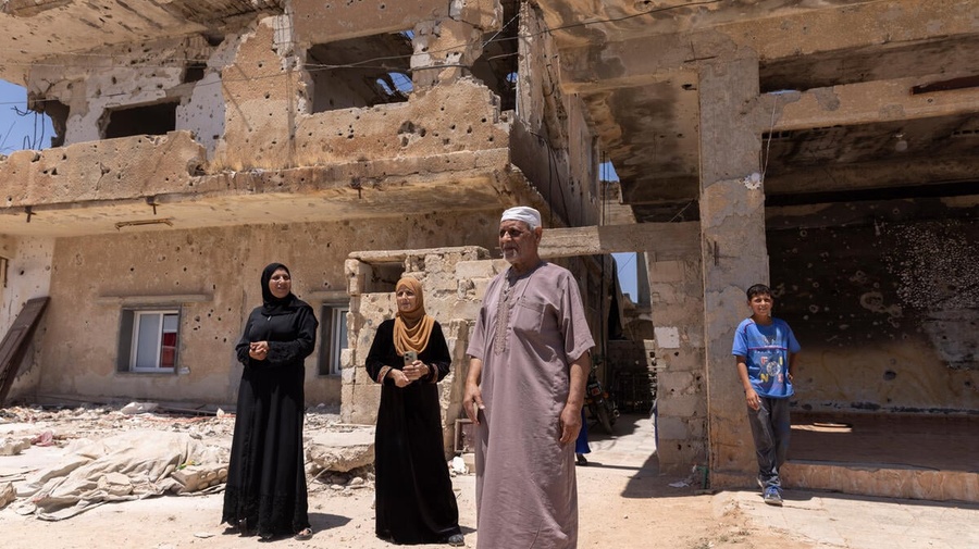 A family of four refugee returnees stand in front of a partially-collapsed building – their home in Daraa, southern Syria