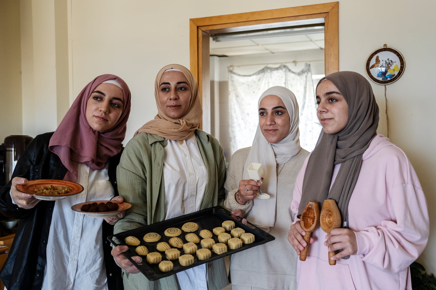 Quatre jeunes femmes portant un foulard tiennent un plateau de biscuits.