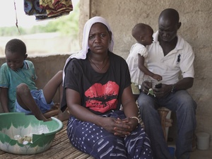 Une femme est assise et regarde la caméra tandis que deux jeunes enfants et un homme sont assis derrière elle