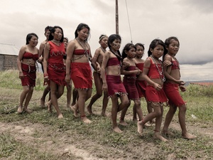 A group of young indigenous people wearing traditional dress walk together near their village