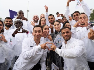 Un groupe de jeunes hommes et femmes vêtus de survêtements blancs font des émojis en forme de cœur avec leurs doigts.