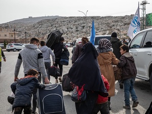 Un groupe de personnes marche sur une route avec leurs affaires, en direction d'un grand rocher.