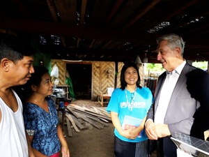 A couple speak to a man in a suit and a woman in a blue UNHCR t-shirt under a shaded area