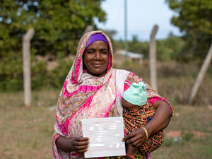 Une femme Pemba du Kenya sourit en tenant un bébé dans ses bras et en montrant fièrement un document.