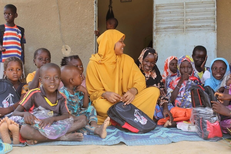 Maimouna (au centre) distribue de nouveaux cartables et du matériel scolaire à des enfants déplacés à Dori, au Burkina Faso.