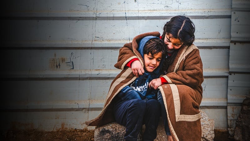 Une jeune réfugiée syrienne s'enveloppe avec son jeune frère dans une couverture alors qu'ils sont assis dehors dans le froid dans le camp de réfugiés de Zaatari.