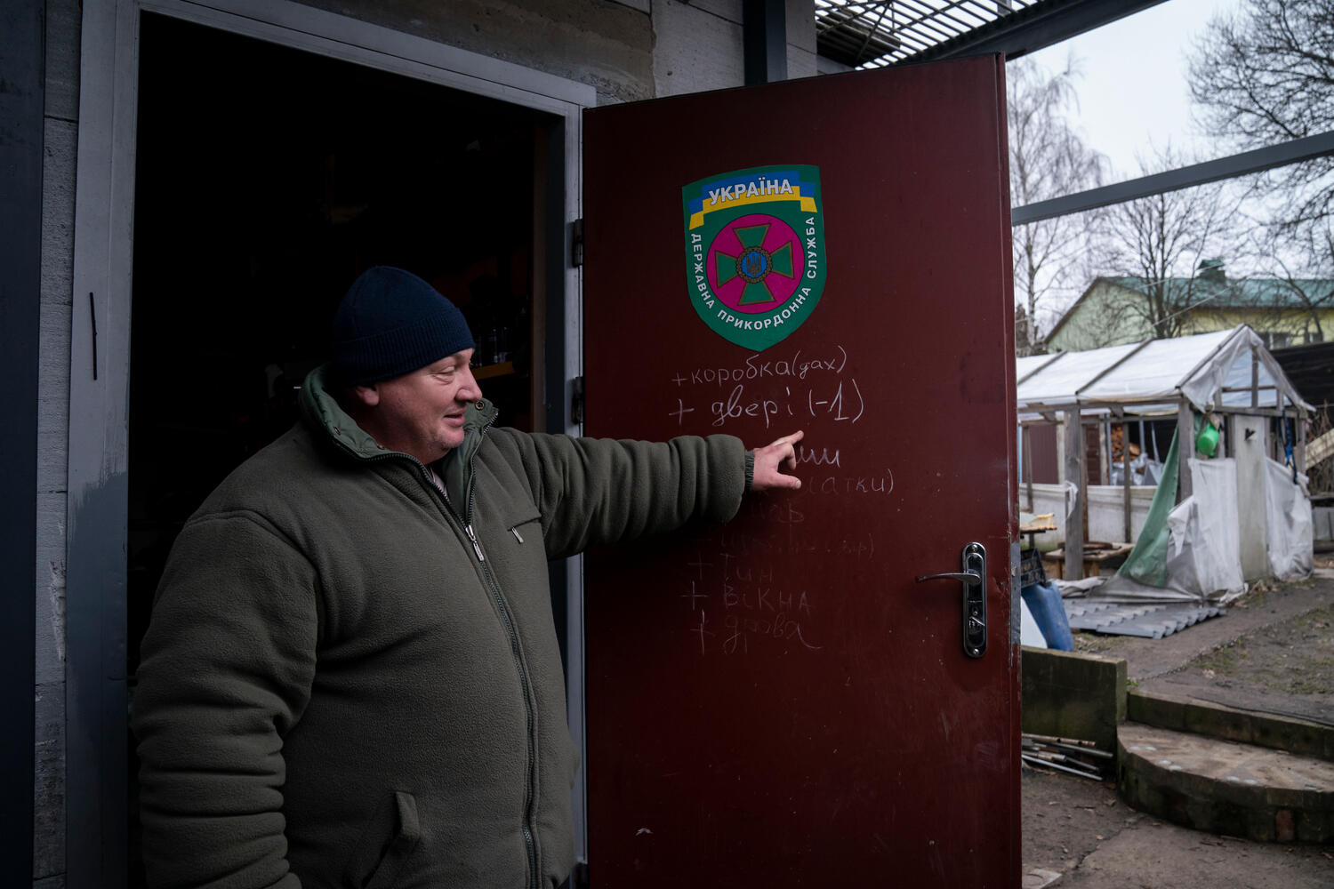 A man points to repair plans written in chalk on the front door of his house.