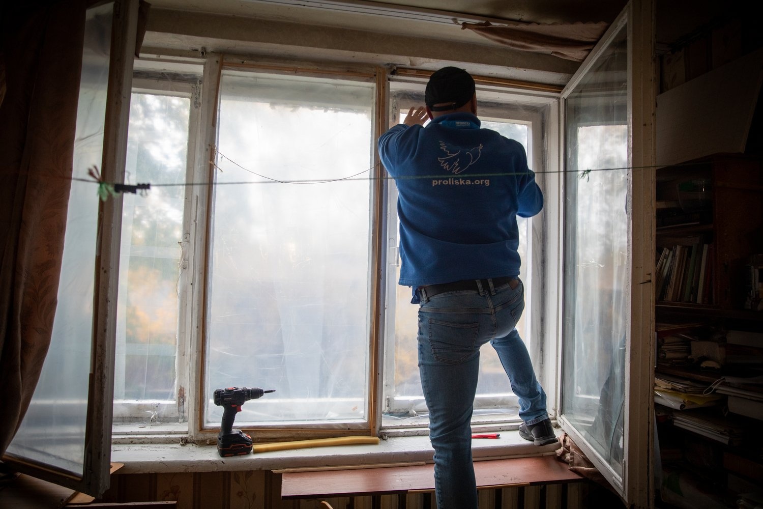 A man stands on an interior windowsill to carry out repairs
