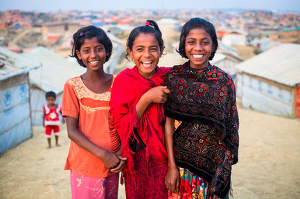 Trois filles sourient à l'appareil photo, dans le camp de réfugiés de Kutupalong.