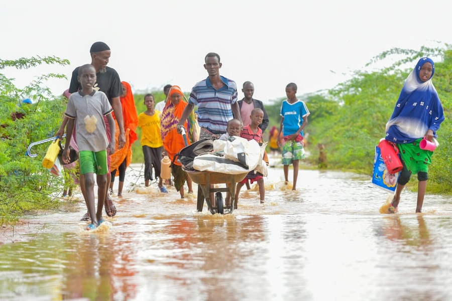 Un homme pousse une charrette à bras contenant un jeune enfant et ses affaires à travers les eaux de crue, accompagné par d'autres membres de la famille.