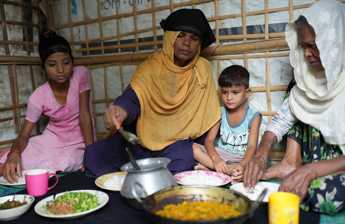 Une mère et une grand-mère mangent assises sur le sol de leur abri avec deux jeunes enfants
