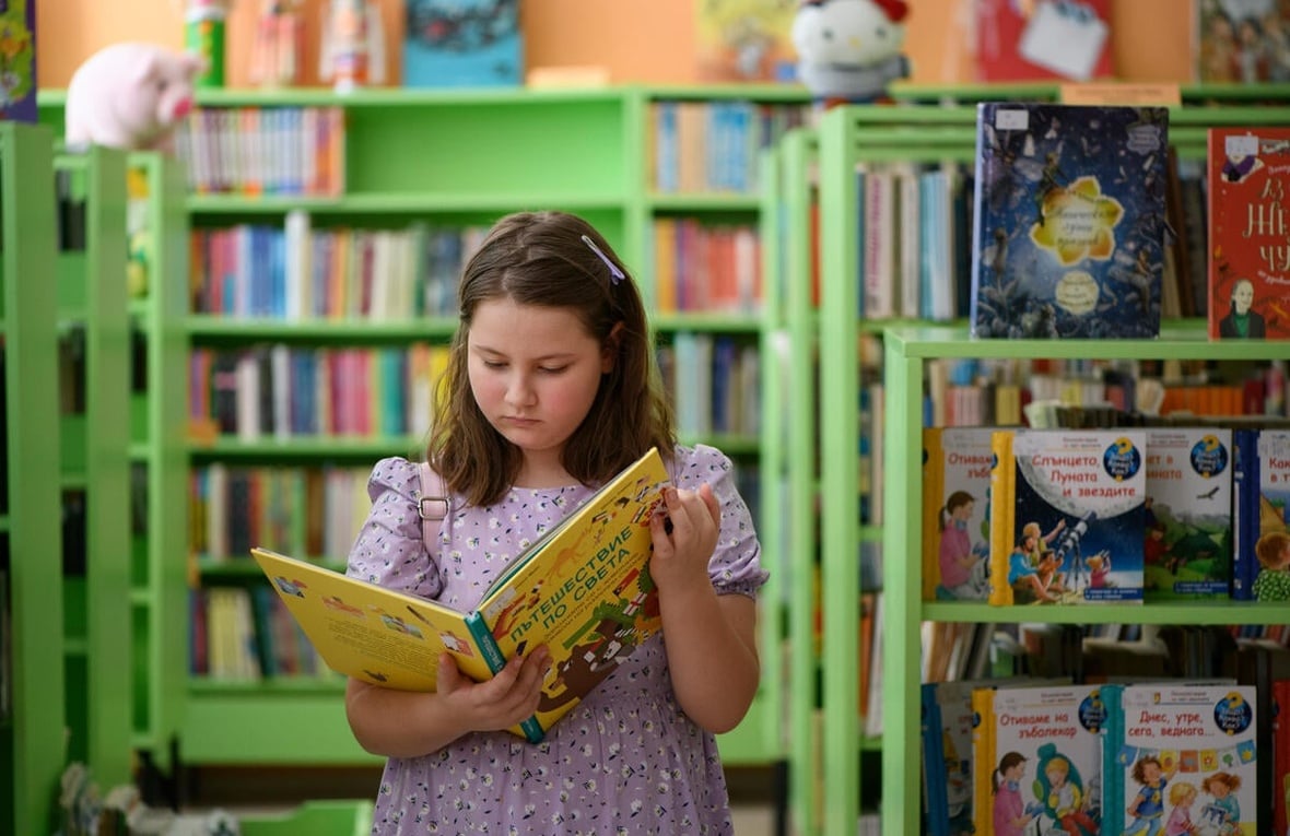 Une jeune fille de 9 ans lit un livre, entourée de livres sur des étagères.