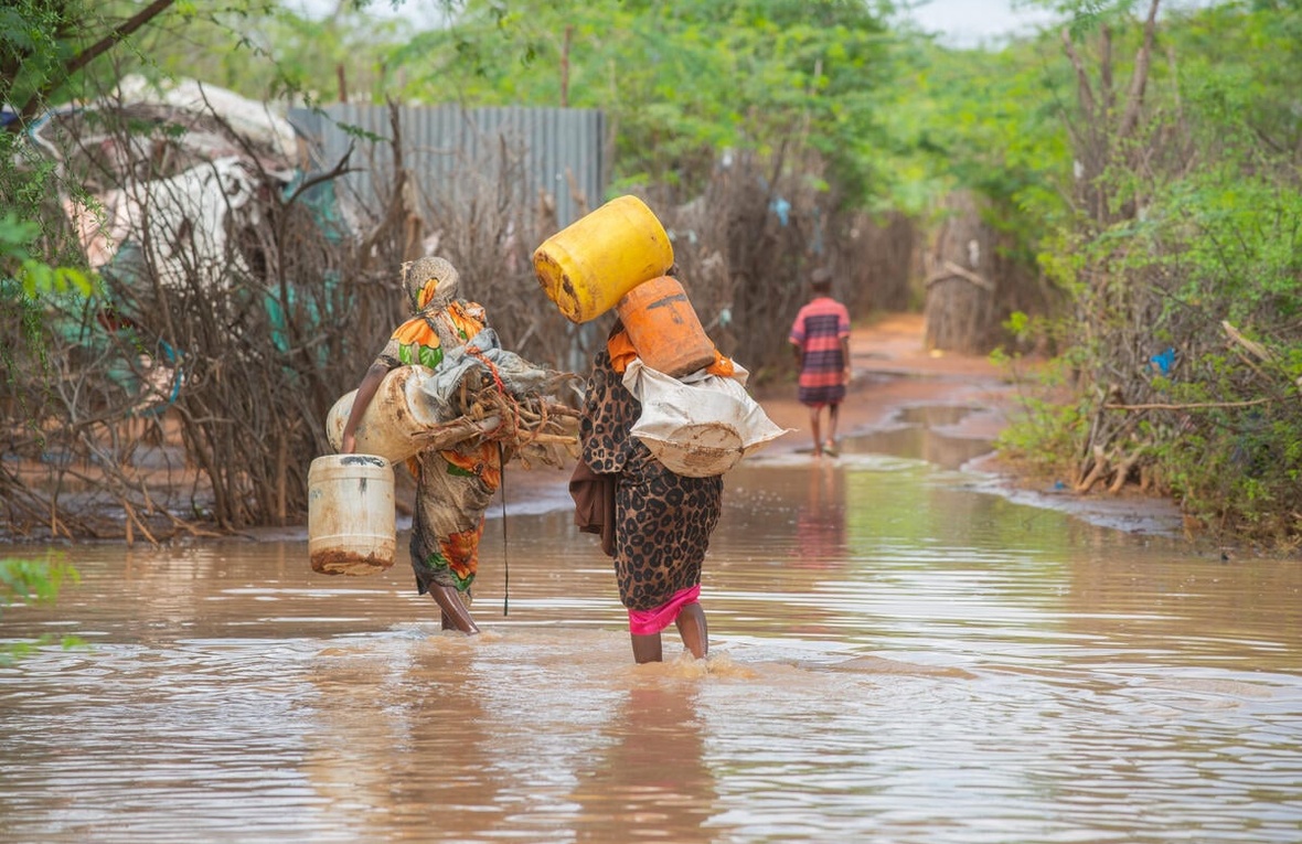 Deux femmes marchent dans une rue inondée en portant des seaux en plastique.
