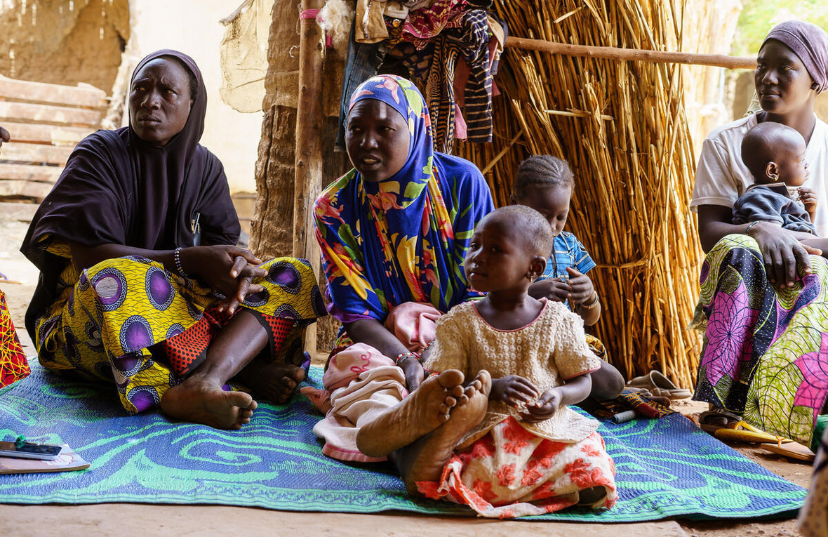Mali. Newly arrived Burkinabe women and children sitting on a plastic mat lent by a member of the host community