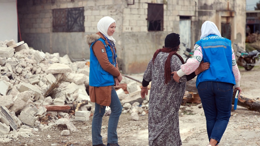 Deux employées du HCR marchent avec une personne déplacée syrienne à côté des débris de sa maison.