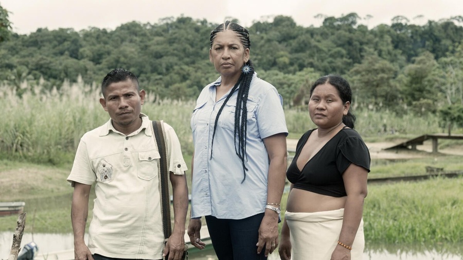 Un homme et deux femmes se tiennent devant un ruisseau à la lisière d'une forêt tropicale. 