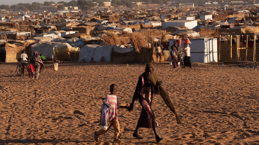 Une femme tient la main d'un enfant alors qu'ils passent devant un campement de réfugiés dans un champ poussiéreux.