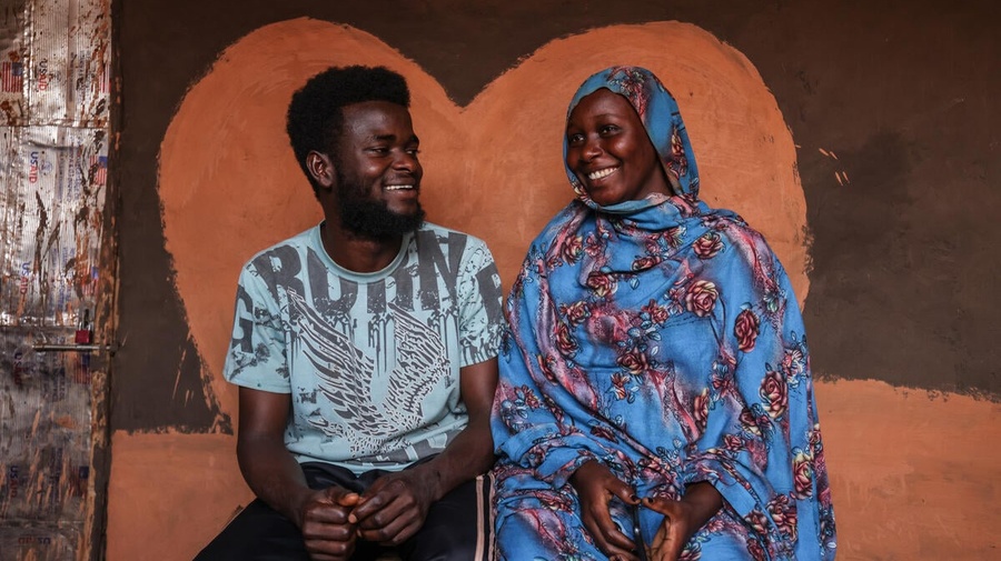 Une femme et un homme sont assis ensemble, se souriant l'un à l'autre, devant une peinture murale en forme de cœur