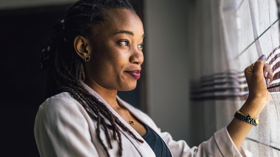 Joséphine pose à côté d'un rideau traversant une fenêtre, la lumière sur son visage.