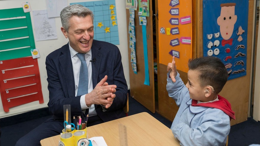Filippo Grandi, Haut Commissaire du HCR, est assis avec un enfant réfugié syrien de 7 ans dans une salle de classe. L'enfant porte une prothèse auditive.