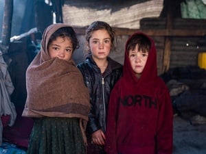 Three children stand outside their shelter in warm clothing and blankets.