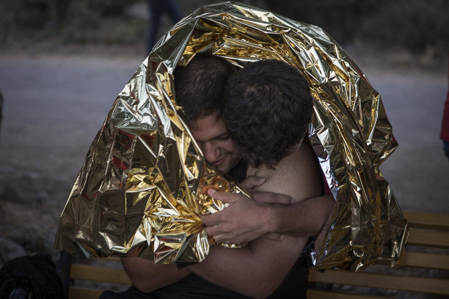 Two Syrian refugees who just landed on Lesvos after a rough crossing from Turkey embrace each other in relief while wearing emergency blankets