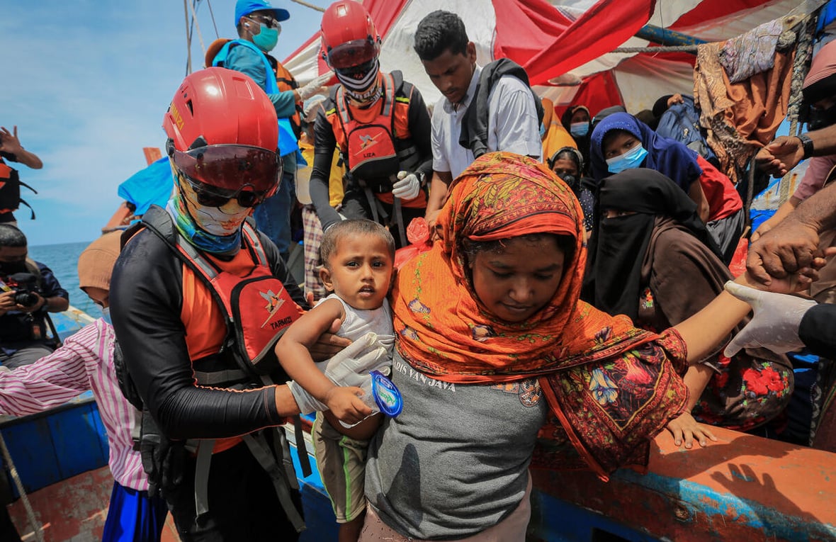 A rescue worker helps passengers disembark from a crowded boat.