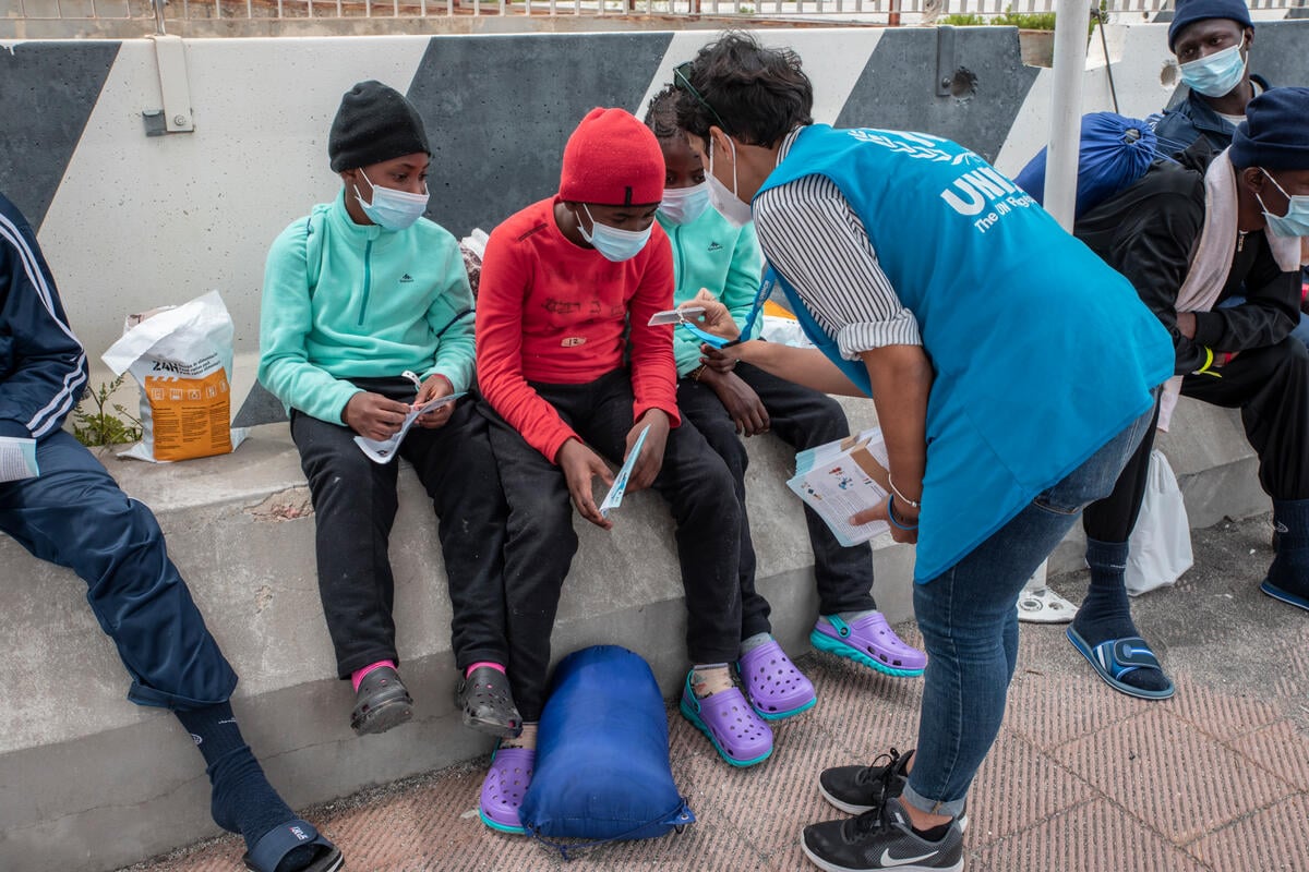 A UNHCR staff member shows her identification to three children