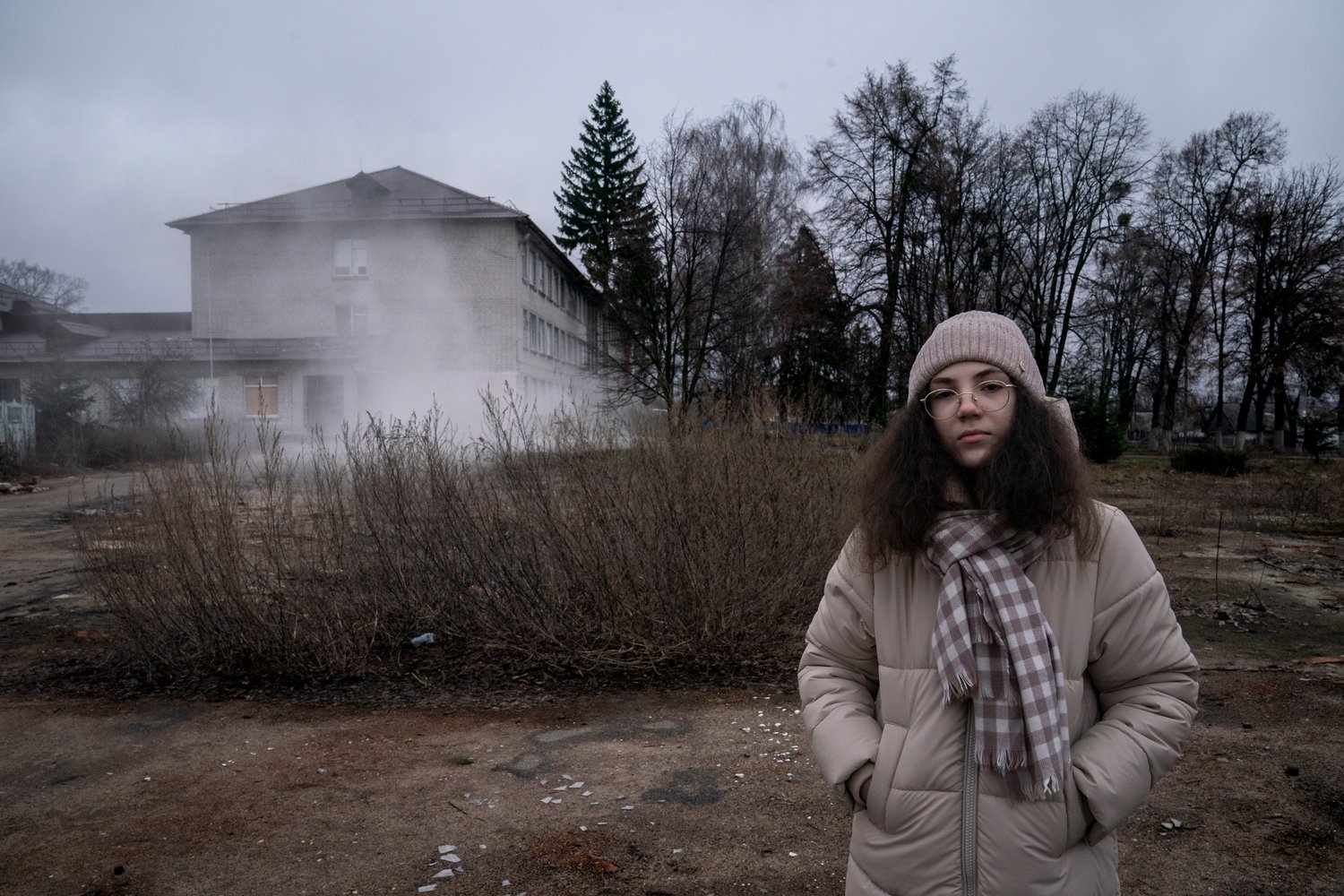 A girl stands in front of a damaged school building.