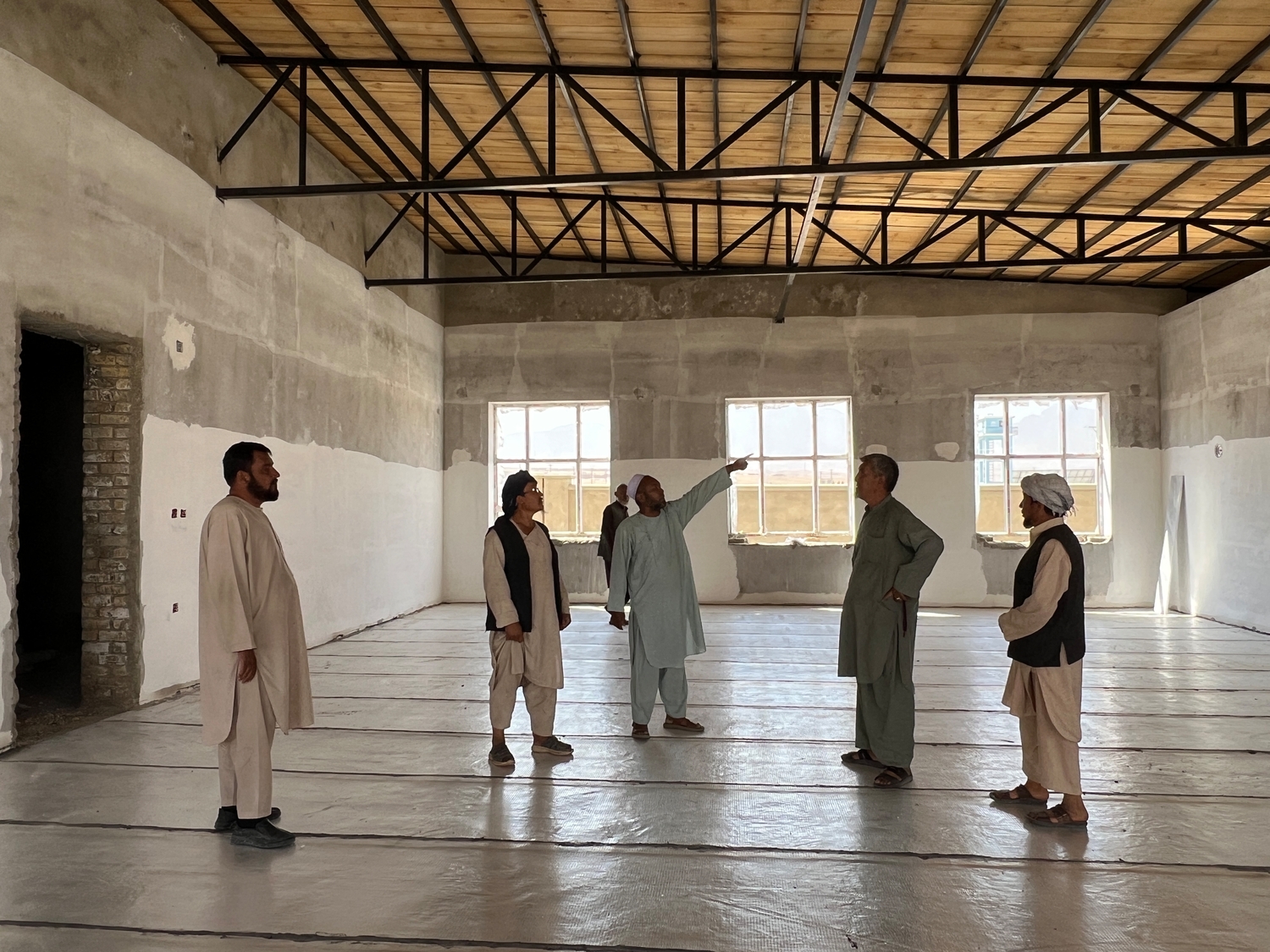 Five man stand in a nearly completed building. A man in the centre is pointing to something off camera.