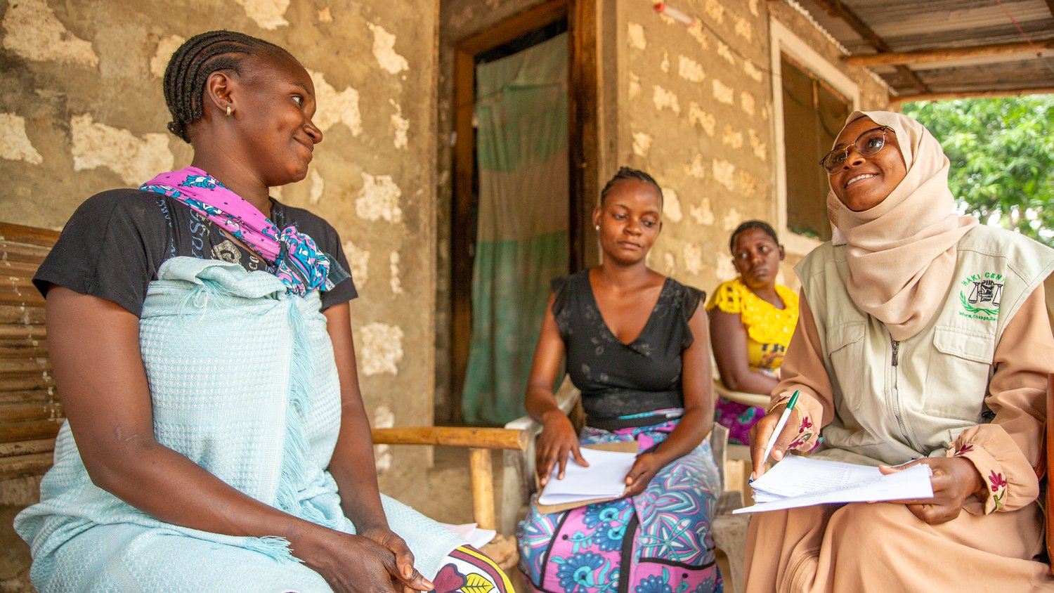 Four women sit on a porch holding some papers.
