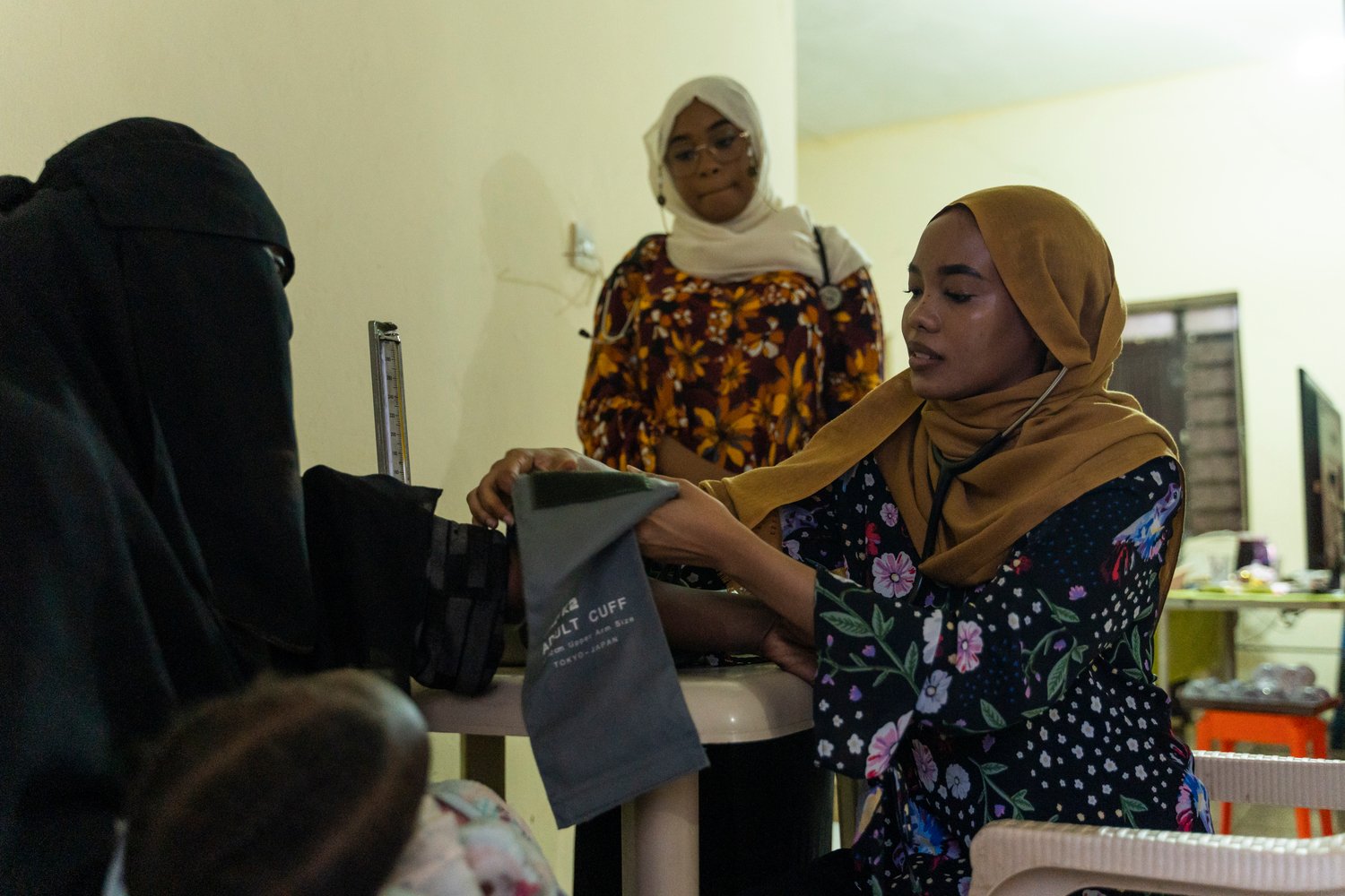 A young woman takes another woman's blood pressure while a third woman looks on.