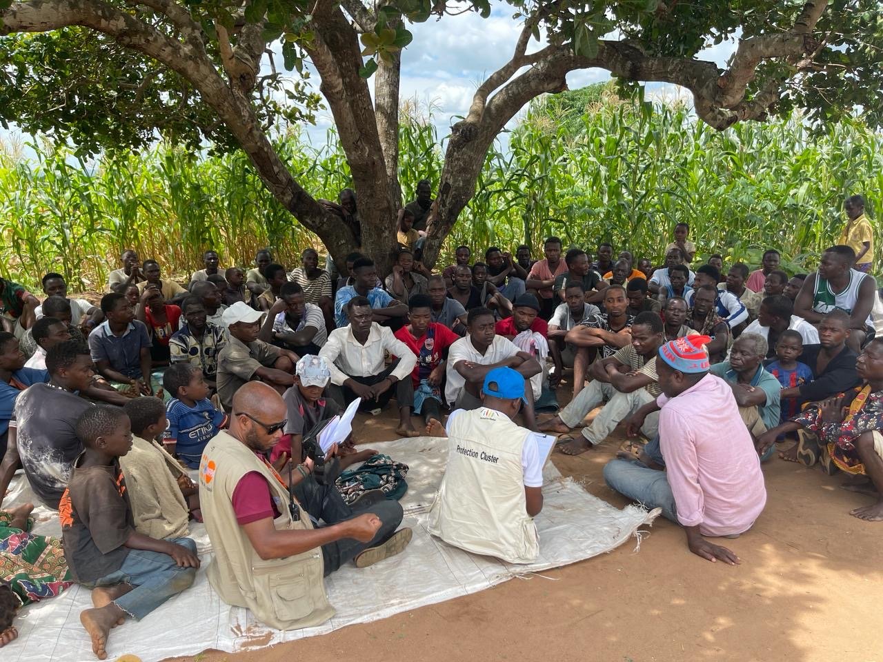 UNHCR staff and refugees sit together under a tree