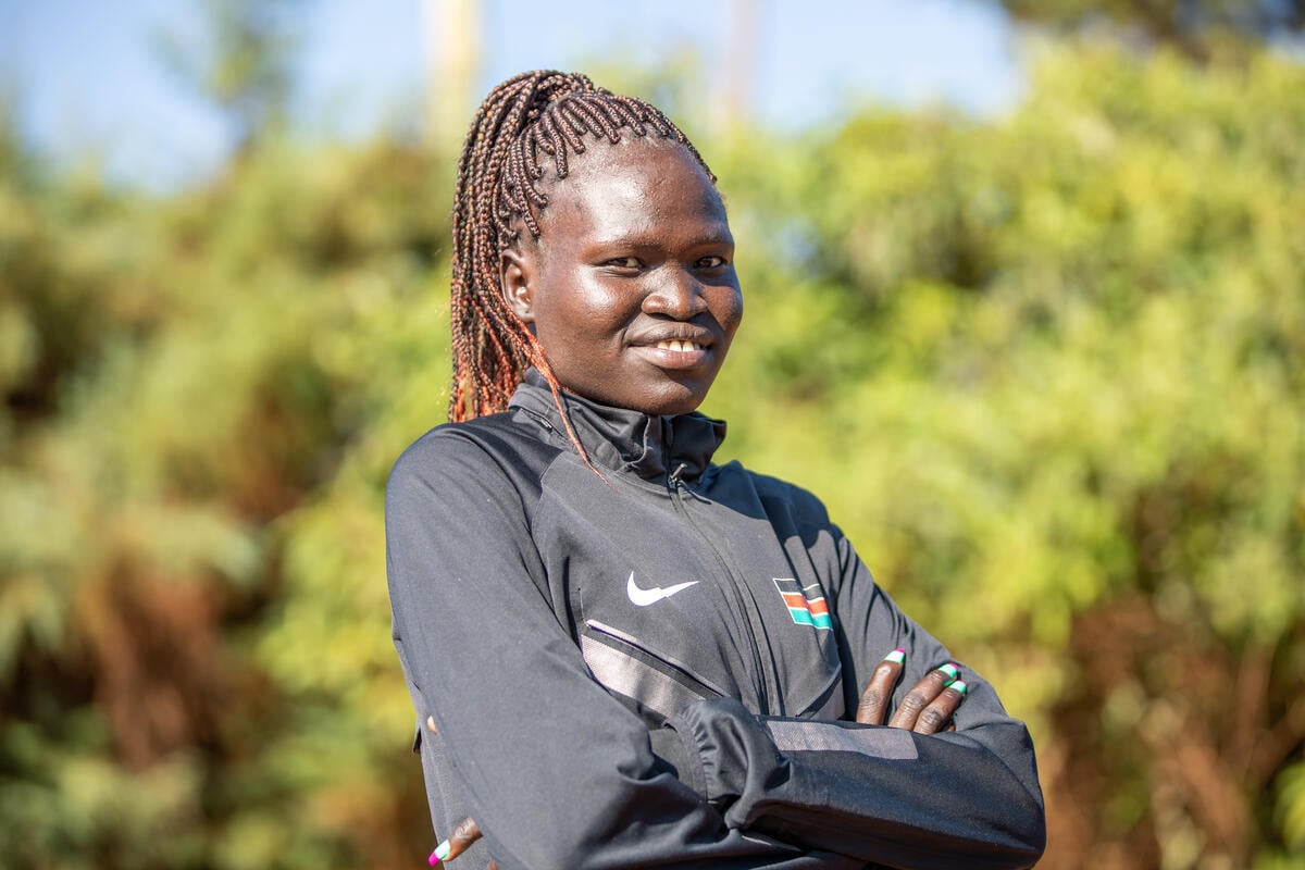 A young African woman wearing a tracksuit poses for a portrait in front of trees.